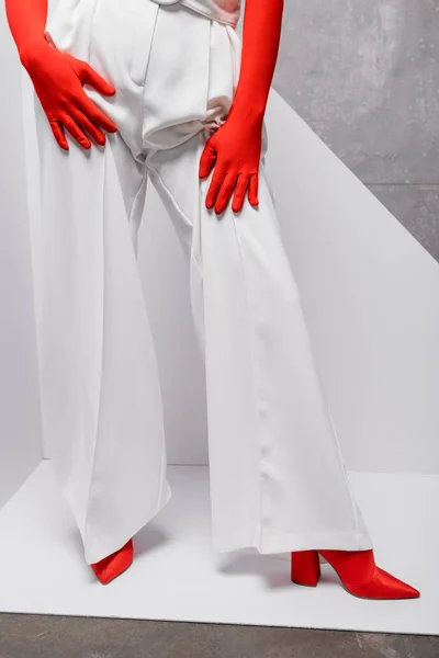 Vue recadrée de femme élégante posant dans des gants rouges et des chaussures sur blanc et gris — Photo de stock