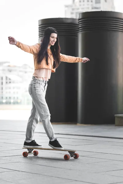 Femme heureuse avec les mains tendues chevauchant sur le skateboard en ville — Photo de stock