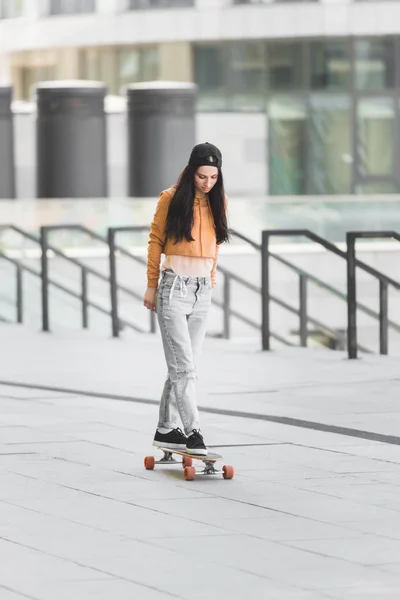 Beautiful brunette woman riding on skateboard in city — Stock Photo