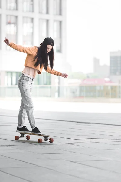 Belle jeune femme avec les mains tendues chevauchant sur le skateboard en ville — Photo de stock