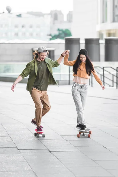 Happy man holding hands with beautiful woman, riding on skateboard in city — Stock Photo