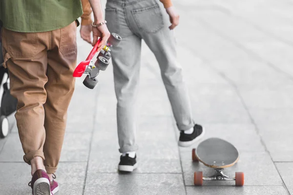 Cropped view of man and woman walking on street with skateboards — Stock Photo