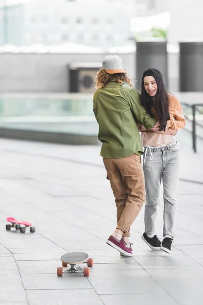 Cheerful woman hugging with man, standing near skateboards in city — Stock Photo