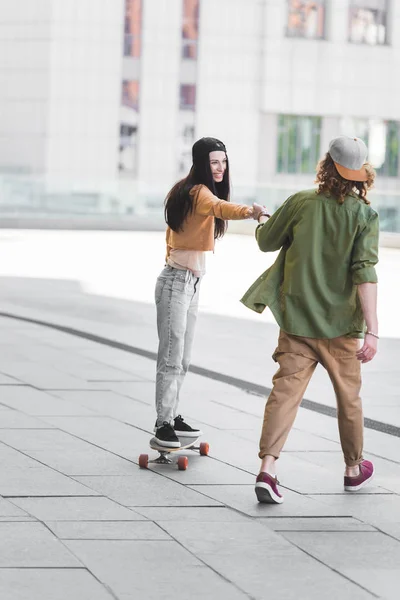 Красивая женщина, держась за руки с мужчиной, катаясь на скейтборде в городе — стоковое фото