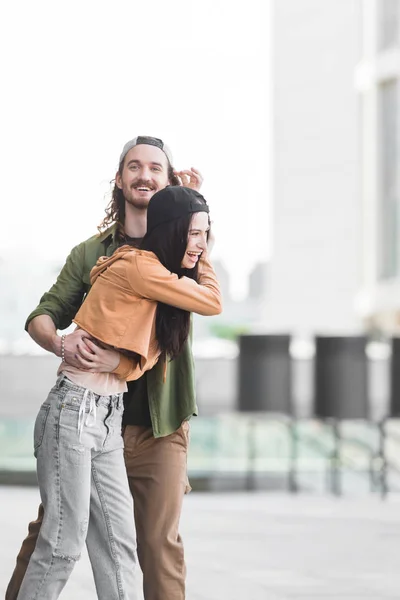 Homem feliz em casual desgaste abraçando com mulher na cidade — Fotografia de Stock