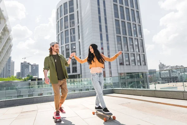 Cheerful woman holding hands with man, riding on skateboard on roof — Stock Photo