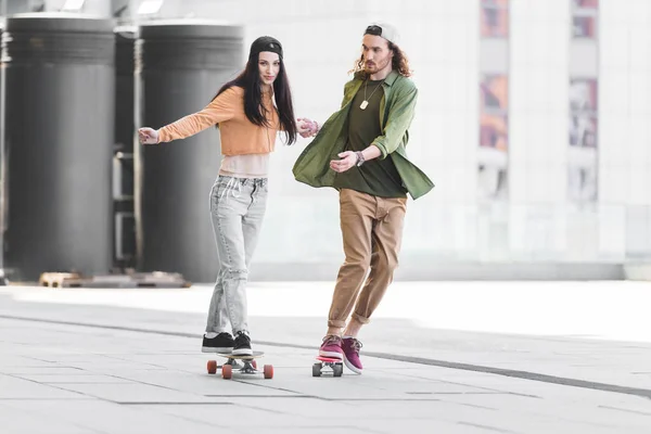 Casal feliz no desgaste casual de mãos dadas, montando em skates na cidade — Fotografia de Stock