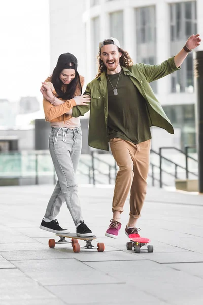 Happy man holding hands with beautiful woman, riding on skateboard in city — Stock Photo