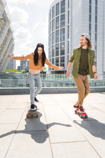 Happy couple in casual wear riding on skateboards on roof — Stock Photo
