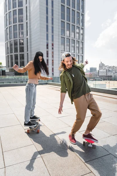 Happy man with beautiful woman riding on skateboards on roof — Stock Photo