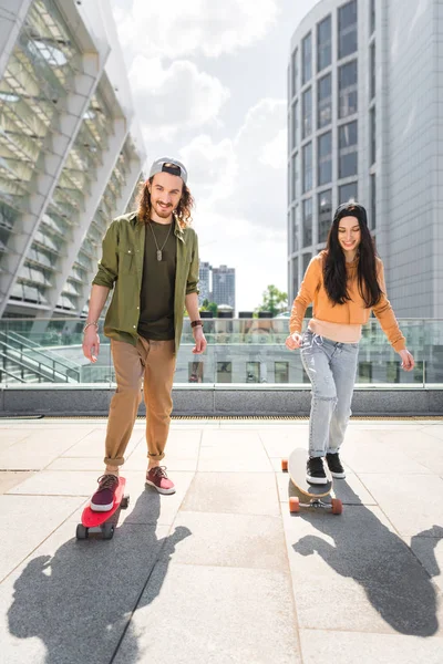 Glücklicher Mann blickt in die Kamera und fährt mit schöner Frau auf Skateboards auf dem Dach — Stockfoto