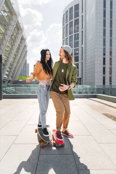 Happy man cuddling to beautiful woman, riding on skateboard on roof — Stock Photo