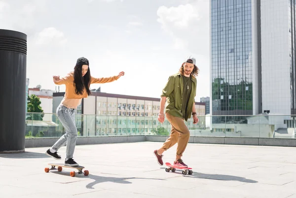 Cheerful woman with man riding on skateboards on roof — Stock Photo