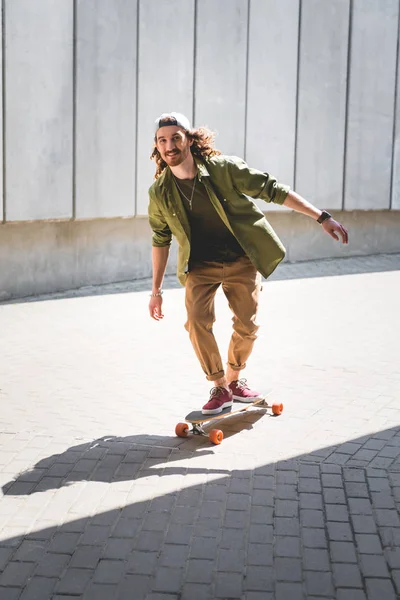 Happy man riding on skateboard near concrete wall, looking at camera — Stock Photo