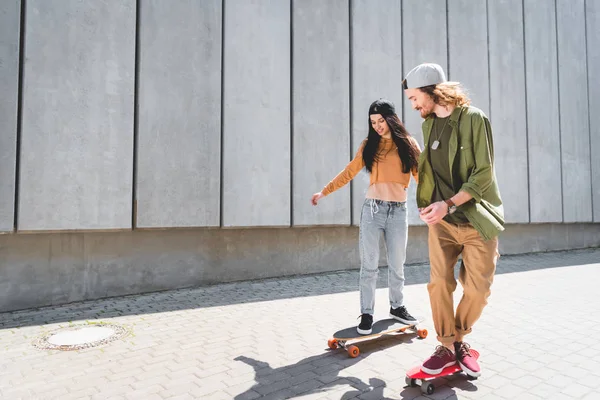 Happy man holding hands with beautiful woman, riding on skateboard near concrete wall — Stock Photo