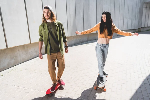 High angle view of man and woman with outstretched hands riding on skateboard near concrete wall — Stock Photo