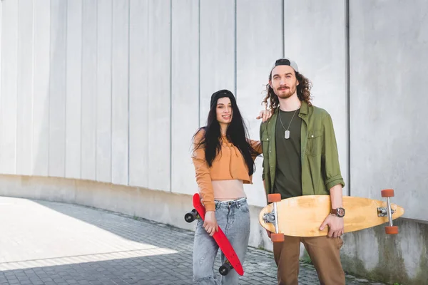 Cheerful woman in casual wear putting hand on man, standing near concrete wall with skateboards — Stock Photo