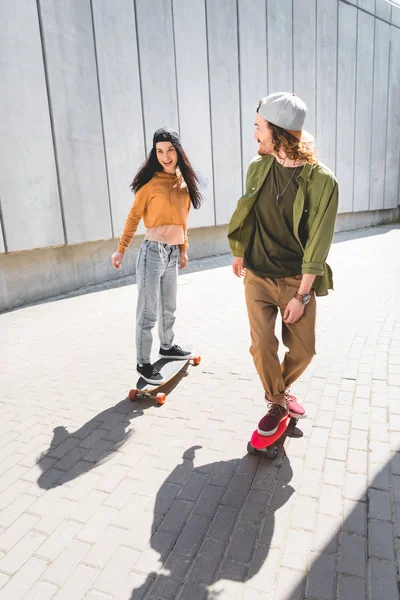 Vista ad alto angolo di felice donna e uomo in abbigliamento casual equitazione su skateboard vicino muro di cemento — Foto stock