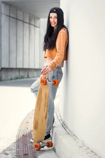 Vista lateral da bela mulher de pé perto da parede concentrado, segurando skate na mão — Fotografia de Stock