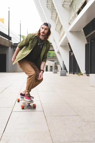 Bonito homem montando no skate na cidade, olhando para longe — Fotografia de Stock