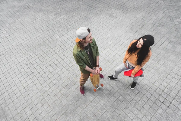 Vista de ángulo alto de hombre alegre y patinadores mujer feliz mirándose, de pie en la calle - foto de stock