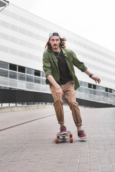 Handsome man in casual wear riding on skateboard, looking at camera — Stock Photo