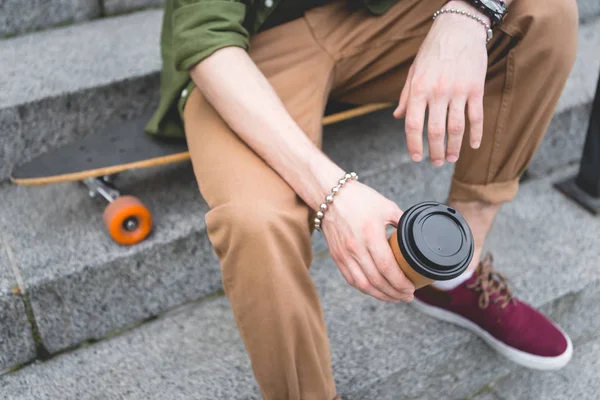 Cropped view of man with paper cup in hand sitting on stairs — Stock Photo