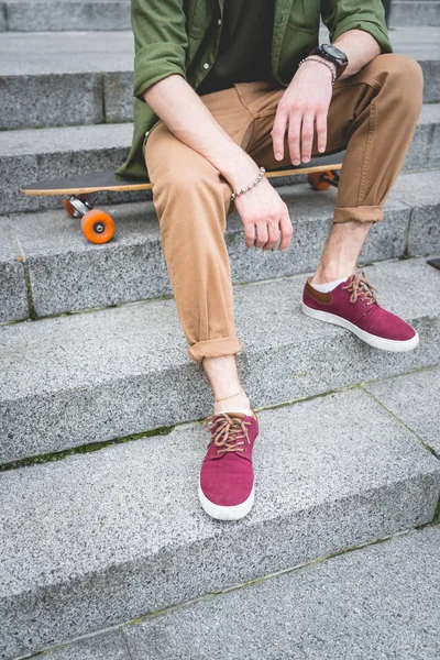 Cropped view of man sitting on skateboard at stairs — Stock Photo