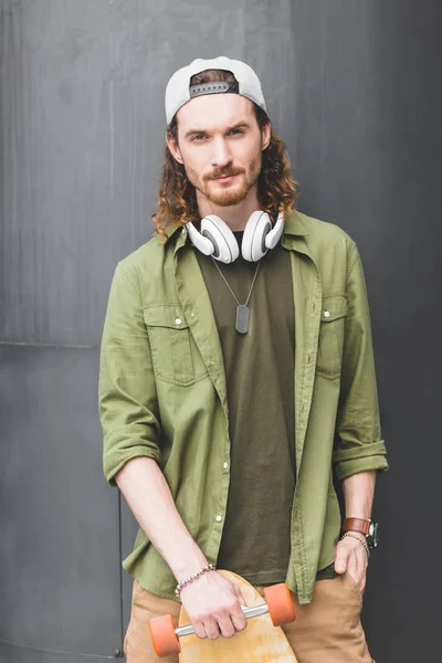 Calm man with skateboard standing on rooftop, looking at camera — Stock Photo