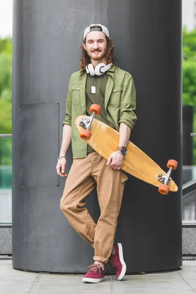 Красивий чоловік тримає скейтборд в руці, стоїть на даху, дивлячись на камеру — стокове фото