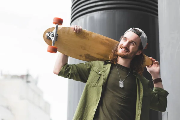 Vista basso angolo di uomo allegro in possesso di skateboard, in piedi sul tetto, guardando altrove — Foto stock