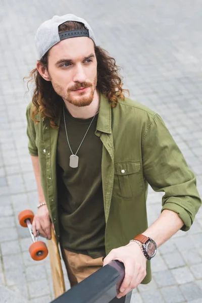 Vista de ângulo alto de homem bonito com skate olhando para longe — Fotografia de Stock