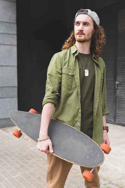 Calm man holding skateboard in hand, looking away — Stock Photo