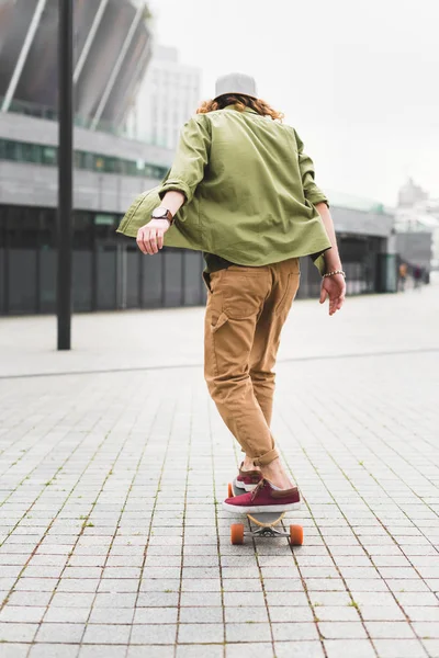 Back view of man in casual wear riding on skateboard at street — Stock Photo