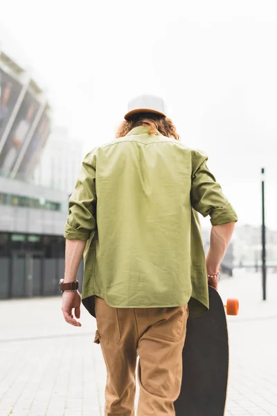 Back view of man in casual wear walking with skateboard in hand — Stock Photo