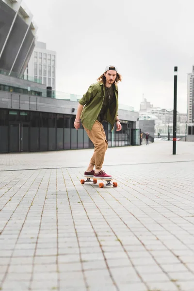 Красивый и спокойный мужчина в повседневной одежде катается на скейтборде, смотрит в сторону — стоковое фото