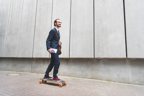 Homem de negócios feliz no desgaste formal montando no skate, olhando para longe — Fotografia de Stock