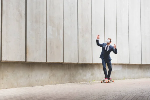 Calm businessman in formal wear and vr headset riding on skateboard, raising hands up — Stock Photo