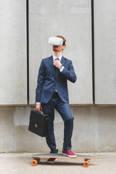 Business man in formal wear and vr headset standing near skateboard with briefcase in hand — стоковое фото