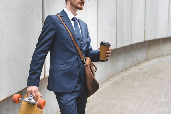 Cropped view of businessman in formal wear holding skateboard and paper cup in hand — Stock Photo