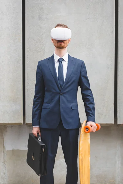 Businessman in formal wear and vr headset holding skateboard and briefcase in hands — Stock Photo