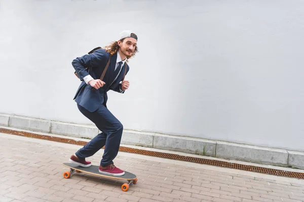 Felice e bello uomo d'affari cavalcando su skateboard in strada — Foto stock