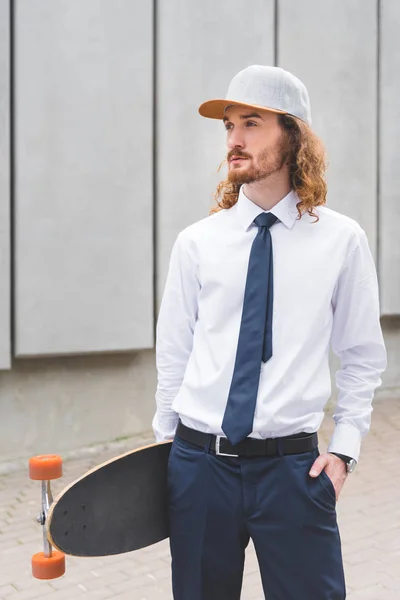 Calm businessman standing with skateboard at street, looking away — Stock Photo