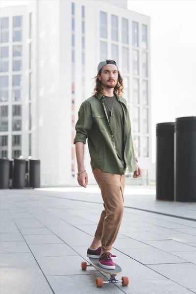 Calm man in casual wear riding on skateboard at street, looking away — Stock Photo