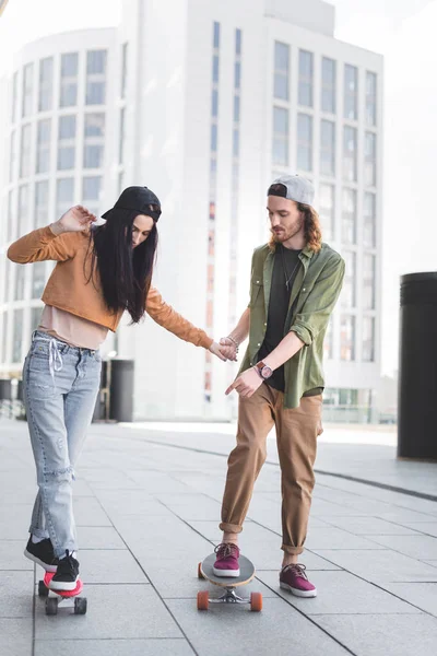 Handsome man holding hands with brunette woman, pointing finger at skateboard — Stock Photo