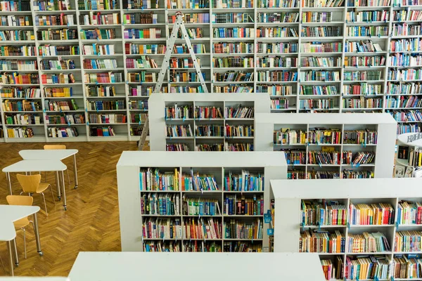 Racks with collection of books near wooden desks and chairs in library — Stock Photo