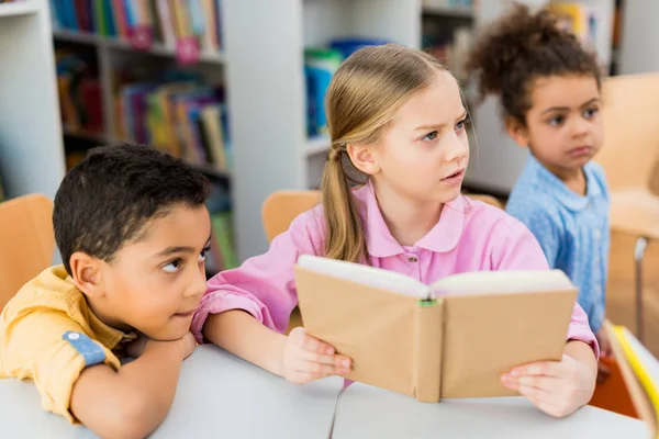 Selective focus of kid holding book near african american children — Stock Photo