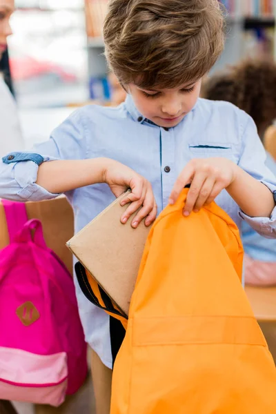 Foco seletivo da criança colocando livro na mochila laranja — Fotografia de Stock