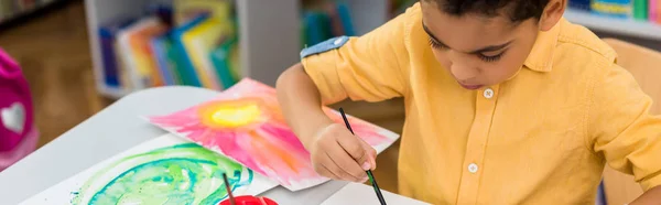 Plano panorámico de la pintura del niño afroamericano mientras sostiene el pincel - foto de stock