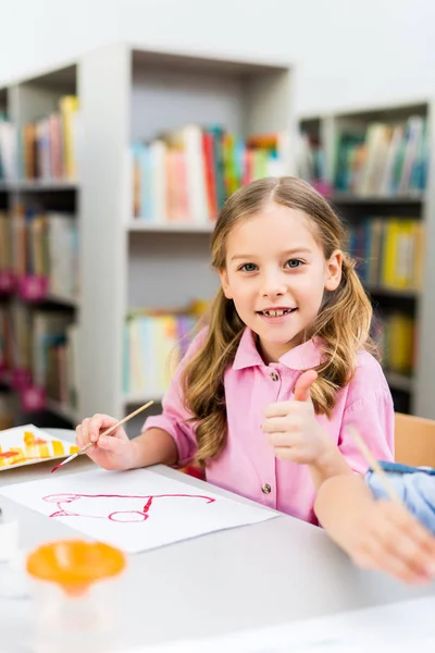 Selective focus of cheerful kid showing thumb up while holding paintbrush — Stock Photo